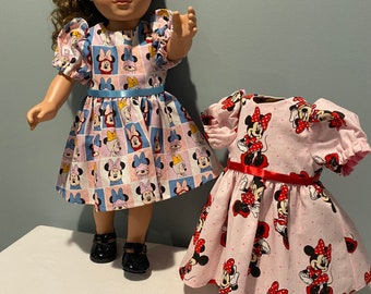 Puede incluir: Dos muñecas con vestidos de Minnie Mouse. La muñeca de la izquierda lleva un vestido azul y rosa con una cinta azul. La muñeca de la derecha lleva un vestido rosa con lunares rojos y una cinta roja.