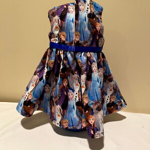 May include: A blue and purple sleeveless dress with a blue ribbon around the waist. The dress is covered in a pattern of characters from the movie Frozen.