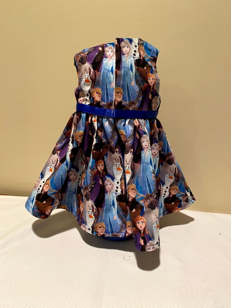 May include: A blue and purple sleeveless dress with a blue ribbon around the waist. The dress is covered in a pattern of characters from the movie Frozen.