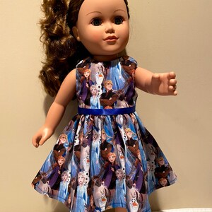 May include: A blue and purple dress with a print of characters from the movie Frozen. The dress has a blue ribbon around the waist and is sleeveless.