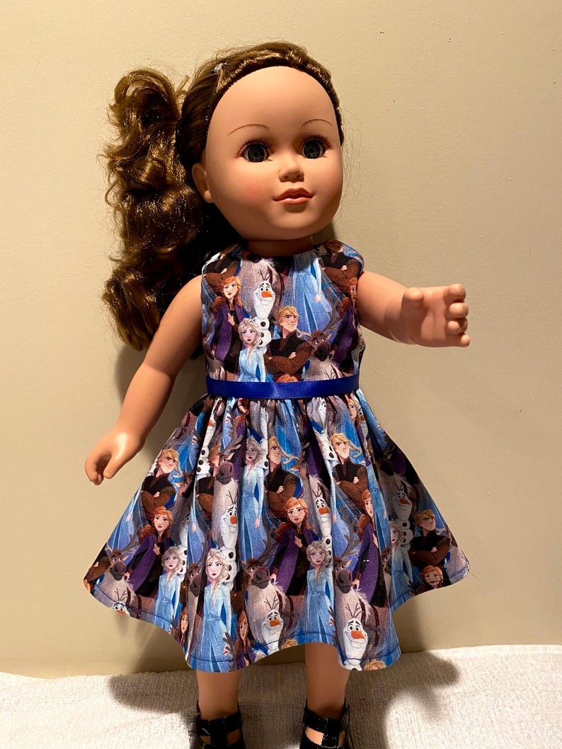 May include: A blue and purple dress with a print of characters from the movie Frozen. The dress has a blue ribbon around the waist and is sleeveless.
