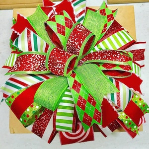 May include: A large, festive bow with a variety of ribbons in red, green, and white. The ribbons feature patterns like stripes, polka dots, and diamond shapes. The bow is likely for a gift or decoration, with a holiday theme.