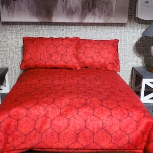 May include: Miniature bedroom set with a red bedspread and matching pillows. Two nightstands with lamps flank the bed. The lamps have gray shades and ornate bases. The room has a gray rug and a neutral-toned wall.
