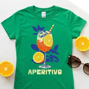 Aperitivo Italian spritz drink shirt flat lay in Irish green — women's Italian summer graphic tee styled with fresh orange slices and sunglasses, cocktail lover gift idea