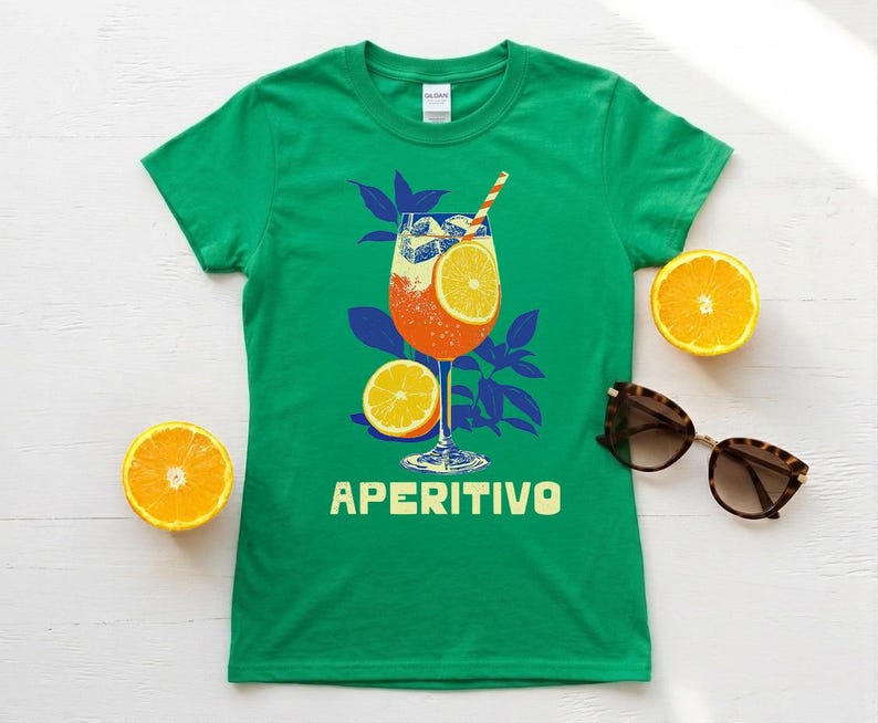 Aperitivo Italian spritz drink shirt flat lay in Irish green — women's Italian summer graphic tee styled with fresh orange slices and sunglasses, cocktail lover gift idea