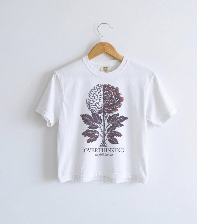 May include: White t-shirt with a graphic of a brain and flower design. The design is split down the middle, with a brain on the left and a flower on the right. The text "OVERTHINKING in full bloom" is below the design.