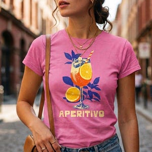 Aperitivo Italian summer shirt in pink worn on cobblestone street — women's semi-fitted graphic tee with vintage spritz cocktail illustration, cocktail lover gift for her