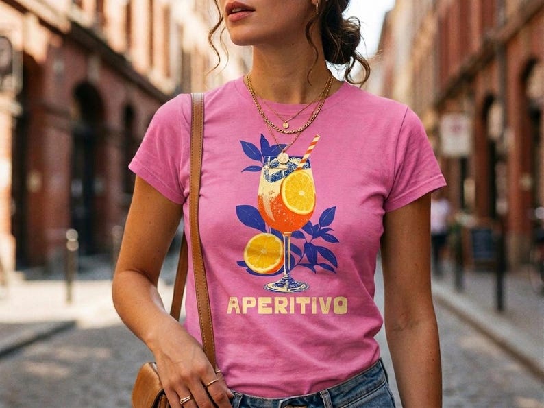 Aperitivo Italian summer shirt in pink worn on cobblestone street — women's semi-fitted graphic tee with vintage spritz cocktail illustration, cocktail lover gift for her