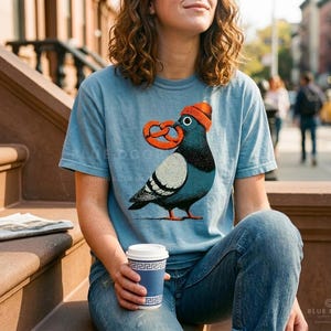 Brooklyn shirt worn on a city stoop with a coffee in hand, ice blue tee with a beanie-wearing pigeon