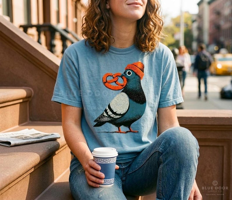Brooklyn shirt worn on a city stoop with a coffee in hand, ice blue tee with a beanie-wearing pigeon