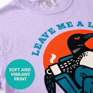 Loon shirt in orchid purple showing close-up detail of the funny bird graphic design, retro illustration of a loon relaxing with coffee, lake house gift tee on garment-dyed Comfort Colors cotton