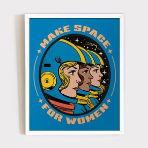 May include: A framed art print featuring three women in space helmets. The image is set against a blue background and includes the text "MAKE SPACE FOR WOMEN" in orange. The women's faces are depicted in a retro comic book style.