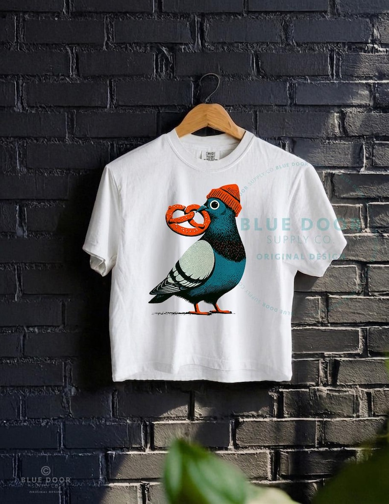 City bird crop in white against a dark brick wall, dopey pigeon in an orange knit beanie