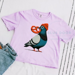 Pigeon crop in orchid styled with folded denim, funny NYC pigeon clutching an oversized soft pretzel