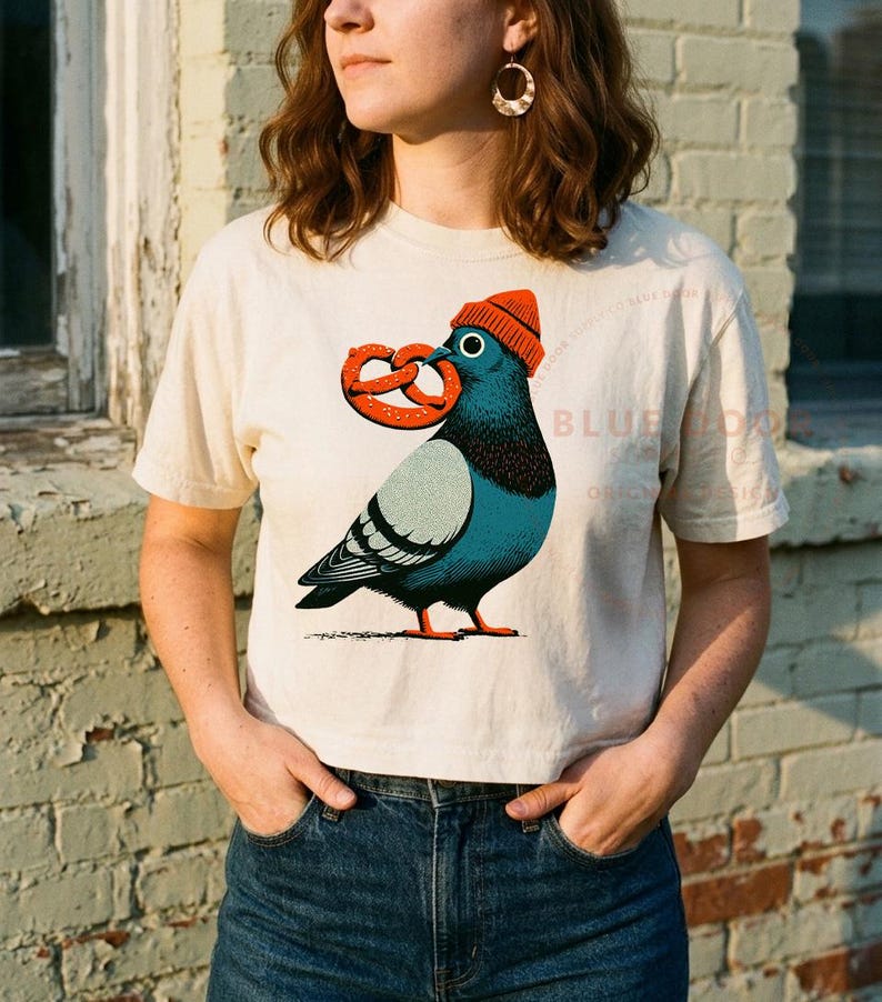 Boxy crop tee worn with jeans against a brick wall, ivory pigeon crop shown candid at 35mm depth of field
