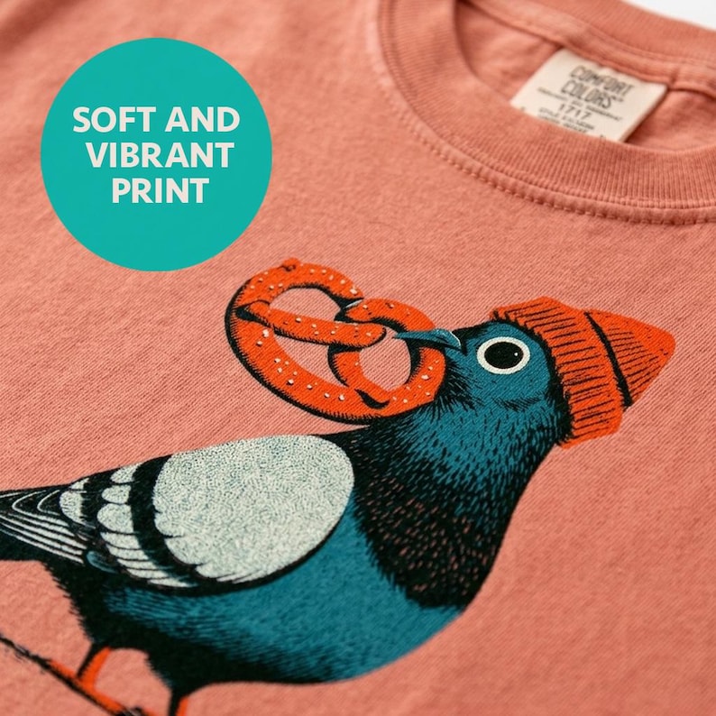 Funny bird shirt in terracotta shown up close, hand-carved block print style line work of a pigeon in a knit hat