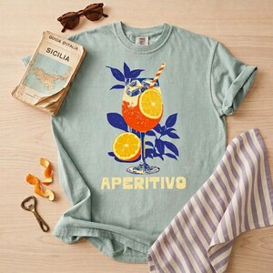 A bay comfort colors tee featuring an italian spritz cocktail and the word Aperitivo below the retro illustrated design.