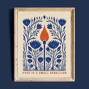 Hope Is A Small Rebellion folk art print framed in light wood on a deep navy wall. Blue and orange wildflower-and-match illustration, a social justice and feminist art print for a gallery wall or activist's home.