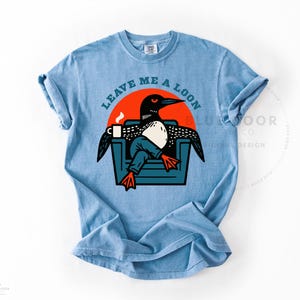 Bird nerd gift shirt in washed denim with a relaxed lived-in drape, funny loon graphic tee on heavyweight Comfort Colors cotton, retro illustration of a loon lounging in an armchair with coffee