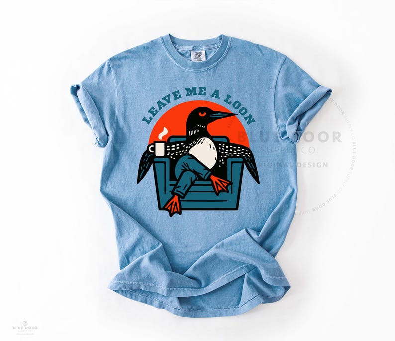 Bird nerd gift shirt in washed denim with a relaxed lived-in drape, funny loon graphic tee on heavyweight Comfort Colors cotton, retro illustration of a loon lounging in an armchair with coffee