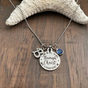 May include: A silver necklace with a charm that reads "I can do all things through Christ who strengthens me". The charm is attached to a silver ball chain with a small blue crystal charm.