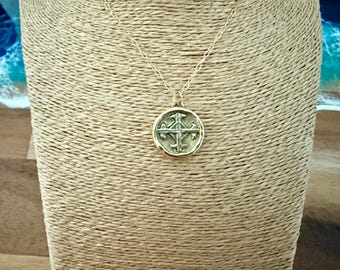 May include: A gold-toned necklace featuring a circular pendant with a raised cross design. The pendant has a textured, antique-style finish and is suspended from a delicate gold-toned chain with elongated oval links, creating a classic look.