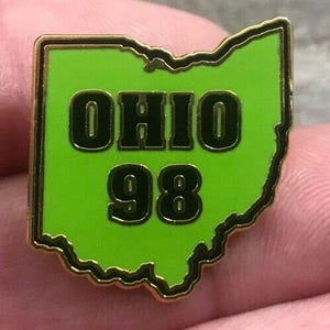 May include: A lime green enamel pin shaped like the state of Ohio with a gold-toned metal border. The pin features the black text OHIO on the top line and the number 98 on the bottom line, both in a bold, block-style font with gold-toned outlines.