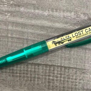 May include: A green pen with a clear barrel and a yellow label that reads "LOST CANYON WISCONSIN DELLS, WIS".