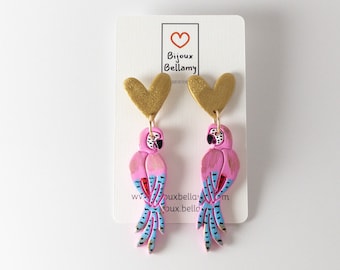 May include: A pair of pink parrot earrings with gold heart accents. The parrots have blue and black striped tails and red accents. The earrings are handmade and feature the text "Bijoux Bellamy".