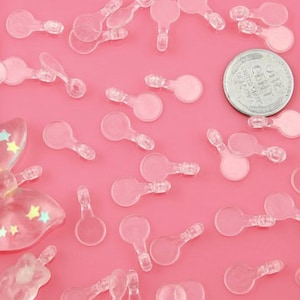 May include: A close-up of a pink surface with many clear plastic round shapes with a small handle. The shapes are scattered across the surface. There is a US coin in the center of the image.