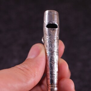 May include: A silver whistle with an ornate design and a red horn-shaped mouthpiece.