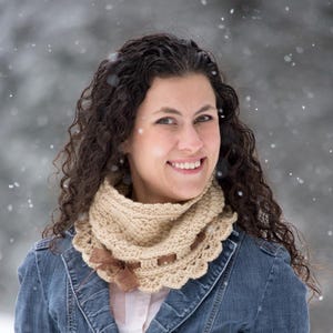 May include: A beige crocheted cowl with a scalloped edge and a brown ribbon woven through the centre, paired with matching beige crocheted fingerless gloves featuring brown ribbon accents, worn over a blue denim jacket and a white shirt.