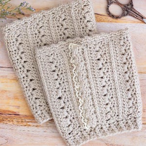 May include: Two beige crocheted items with intricate patterns and a delicate lace trim. The items are rectangular and appear to be handmade. The background includes a wooden surface, a ball of yarn, and vintage scissors.
