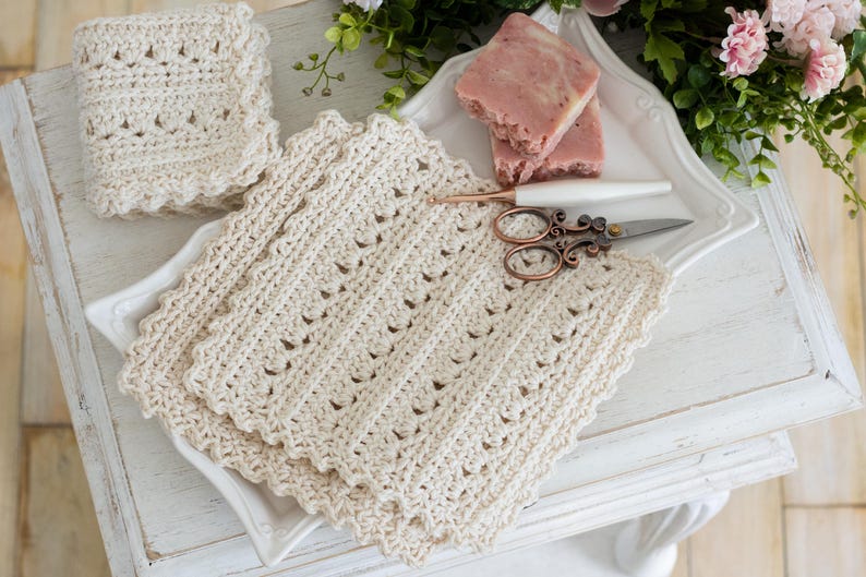 Crochet Primrose and Proper dishcloth with scissors, soap, crochet hook, flowers, and white tray on a wood surface.