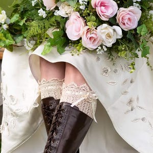 Könnte beinhalten: Eine Braut in einem weißen Kleid mit Spitzendetails und braunen Lederstiefeln mit Spitzenbesatz. Sie hält einen Strauß rosa Rosen und Grünzeug.