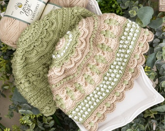 May include: Two crocheted hats featuring intricate textured patterns. One hat is solid sage green, while the other combines beige, sage green, and white. Both hats have scalloped edges and are displayed with two skeins of Yarn Bee Yarntopia ivory yarn.