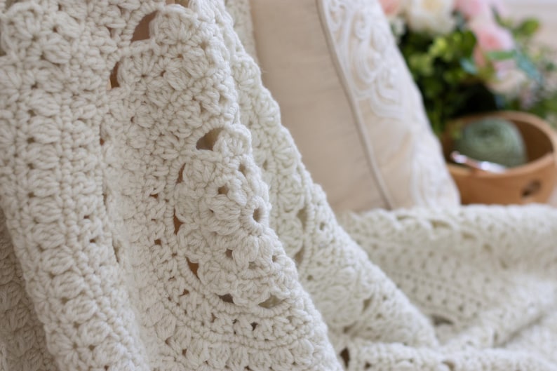 May include: A cream-colored crochet blanket featuring a repeating circular fan pattern with textured stitches. The fabric is thick and soft, showcasing intricate hand-stitched details throughout the entire surface of the textile throw.