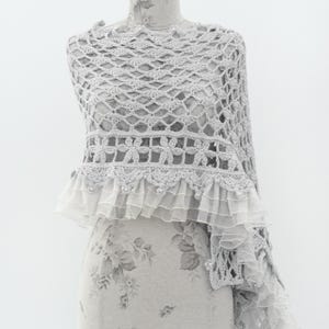 May include: A gray crochet shawl with a delicate ruffle trim. The shawl is made with a lacy pattern and features small pearl-like beads.