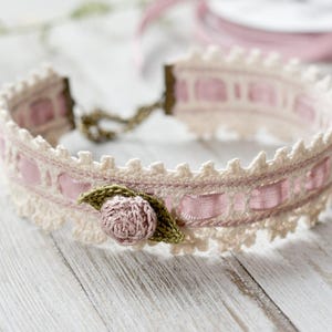 May include: A delicate crocheted choker necklace with a pink satin ribbon and a small crocheted rose.