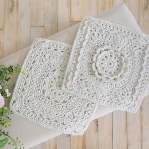 May include: Two off-white, square crochet doilies with intricate floral and geometric patterns. The doilies are placed on a neutral-colored surface, showcasing the detailed texture of the handmade pieces. The crochet work features a central floral motif and a scalloped edge.