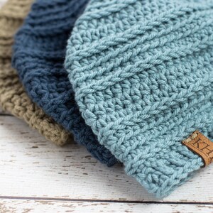 May include: Three crocheted beanies in different colors: green, blue, and light blue. The light blue beanie has a brown leather tag with the word "KHL" on it.
