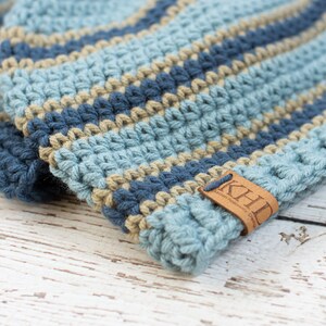 May include: A blue and tan striped crocheted beanie with a brown leather tag that says "KHD Leather Handmade Goods".