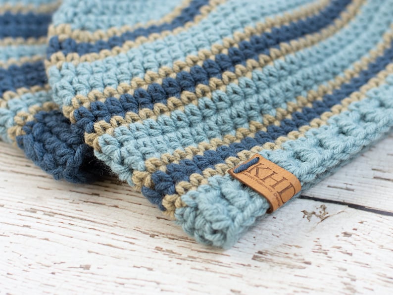 May include: A blue and tan striped crocheted beanie with a brown leather tag that says "KHD Leather Handmade Goods".