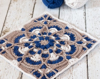 Könnte beinhalten: Ein quadratisches Häkelmotiv mit einem komplexen, von Mandalas inspirierten Muster aus marineblauem, beigem und weißem Garn. Das Design umfasst Reliefmaschen und komplizierte geometrische Formen, die von der Mitte ausgehen, mit weißem Rand.