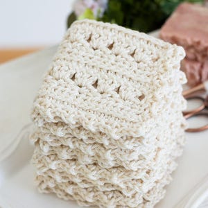Primrose and Proper crochet cream dishcloth on a white dish with flowers in the background.