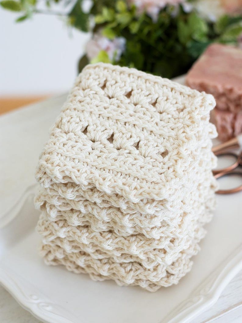 Primrose and Proper crochet cream dishcloth on a white dish with flowers in the background.