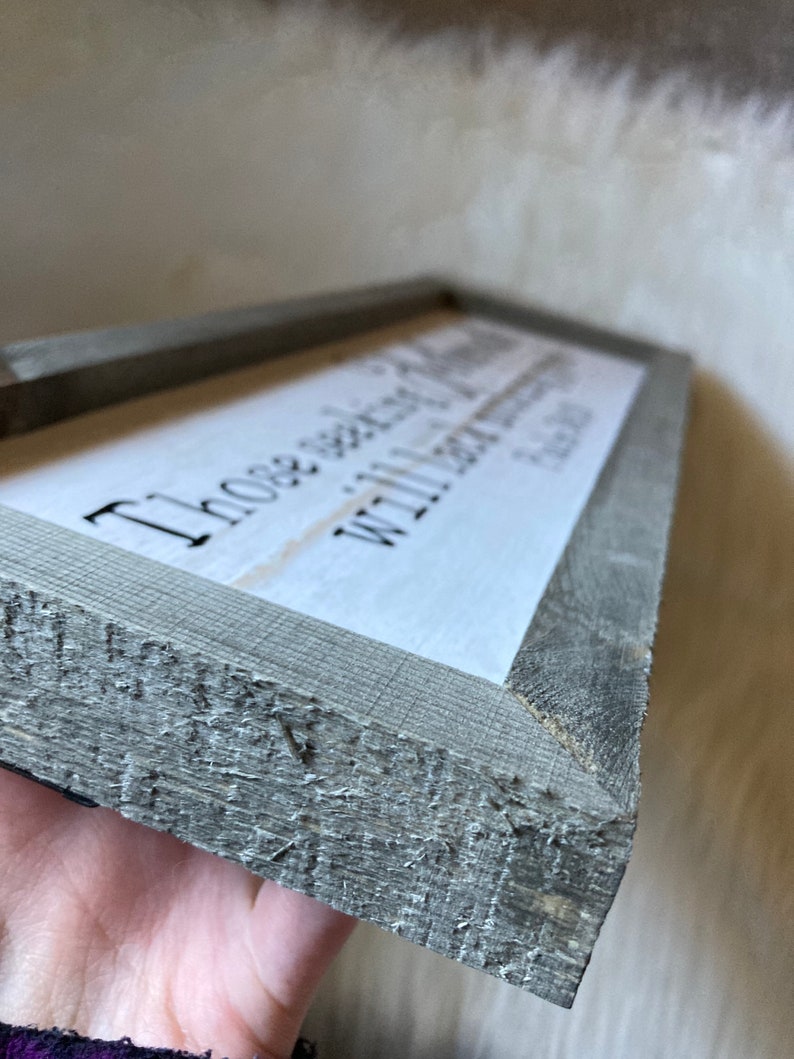 May include: A rustic wooden sign with a gray stain and a white background. The sign reads "Those who wander are not lost, with love always find your way home".