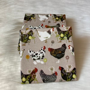 May include: Two square ceramic coasters with a beige background and a repeating pattern of black, white, and brown chickens, green leaves, and white flowers.