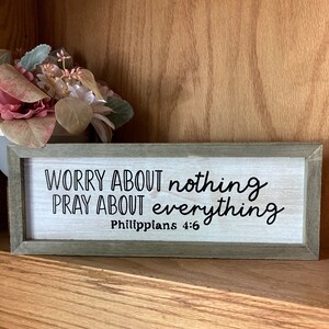 May include: A wooden sign with the text "WORRY ABOUT nothing PRAY ABOUT everything Philippians 4:6" in black lettering on a white background.