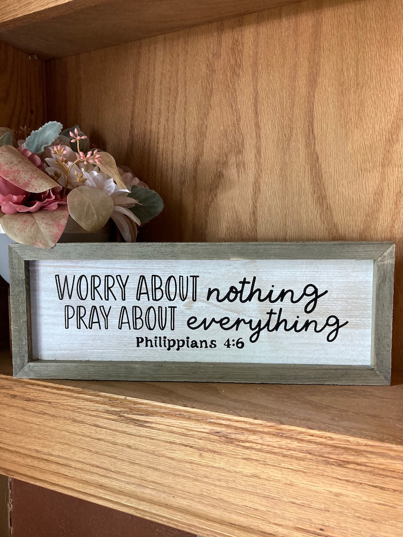 May include: A wooden sign with the text "WORRY ABOUT nothing PRAY ABOUT everything Philippians 4:6" in black lettering on a white background.